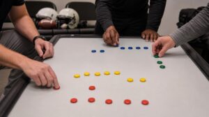 Hands arrange colored markers on a blank board during a football league planning meeting