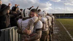 Muddy American football players celebrating promotion with supporters